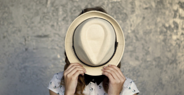 A woman holding a hat to cover her face.